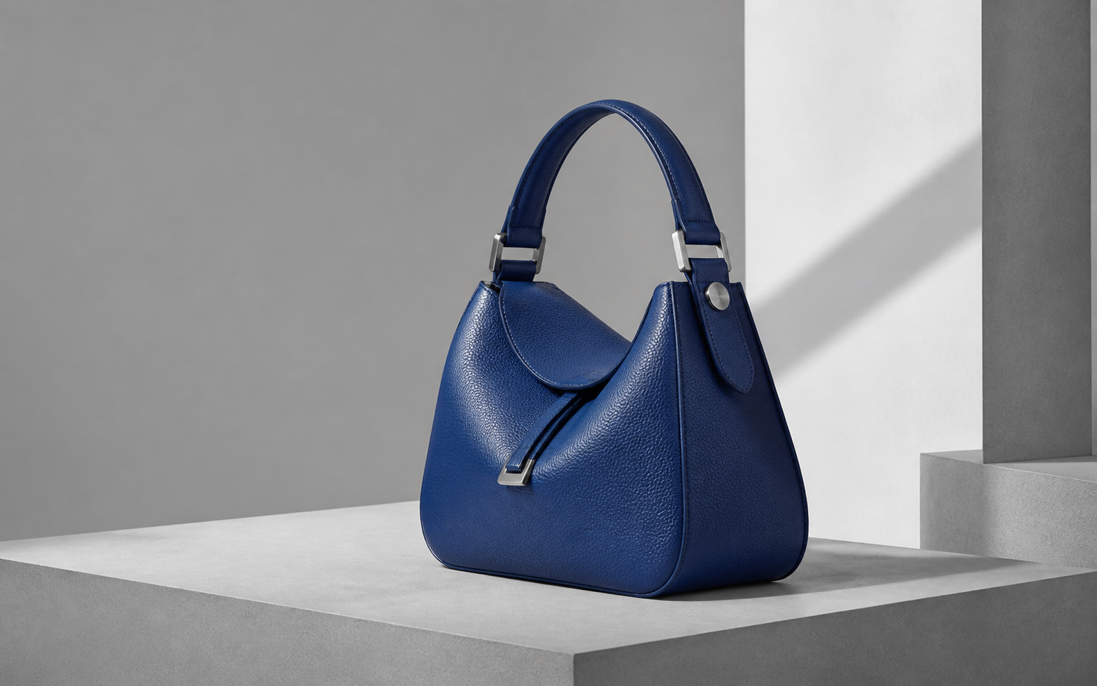 A sculptural cobalt leather handbag on a pale architectural plinth